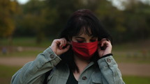 a woman standing outdoors putting on a face mask 