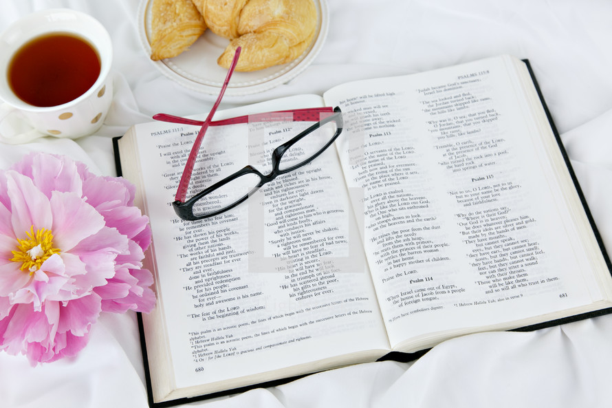 reading glasses, croissant, tea cup, open Bible, and pink flower 