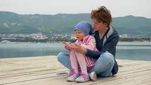 Little girl sits in a woman's lap on a dock. 