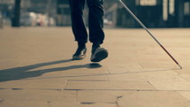 a blind man using a walking stick to walk on a public sidewalk 