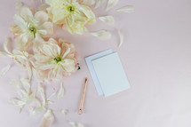 stationary, pen, and flower petals on a pink background 