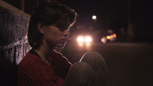 scared young woman sitting alone outdoors in a city at night 