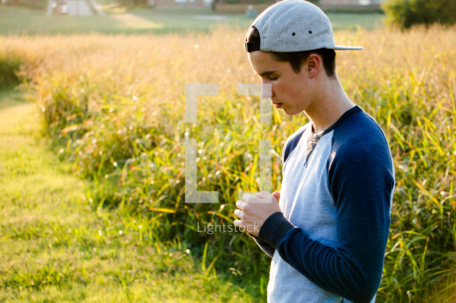 a teenage boy praying outdoors 