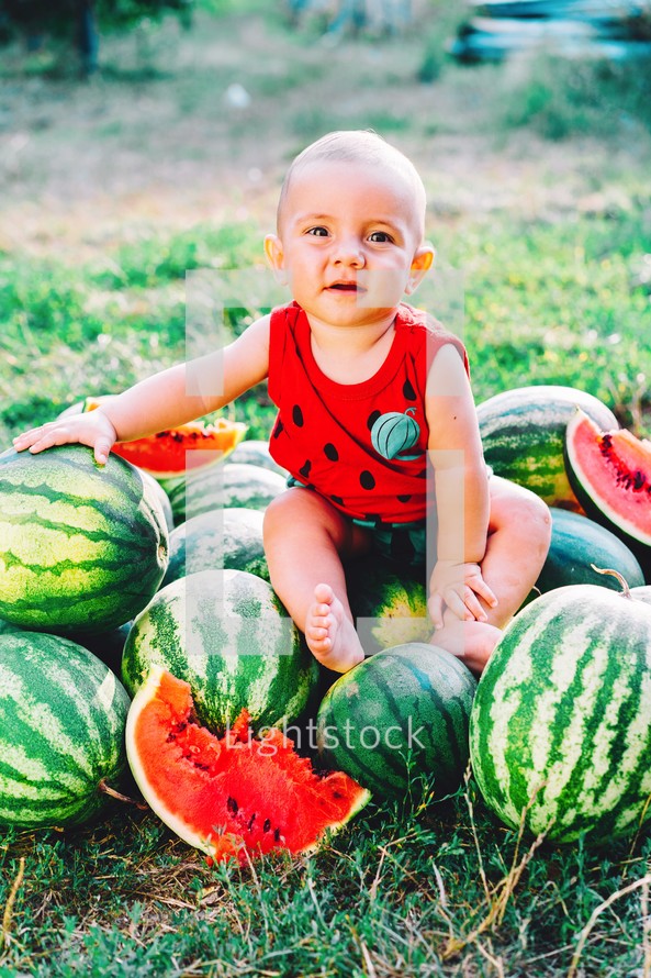 Happy little baby boy in funny costume sitting and eating slice of watermelon on field or garden. Happy Infant child smiling. Kid eat fruit outdoors