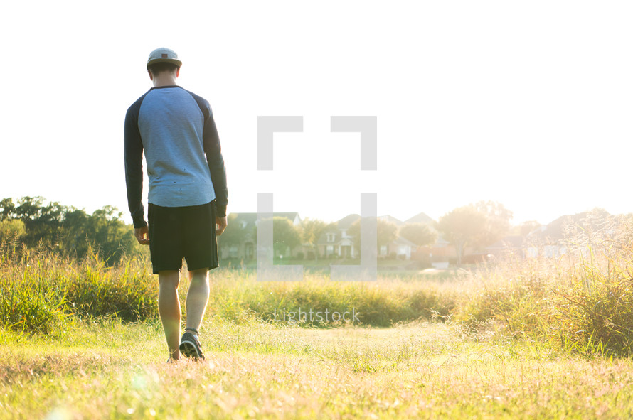 a teen boy walking through a field alone 