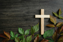 wooden cross and red and green leaves on a wood background 