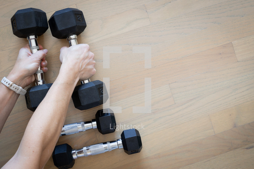 Woman's hands picking up dumbbells