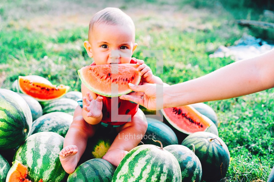 Happy little baby boy in funny costume sitting and eating slice of watermelon on field or garden. Happy Infant child smiling. Kid eat fruit outdoors