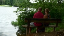 couple sitting on a park bench by a lake 