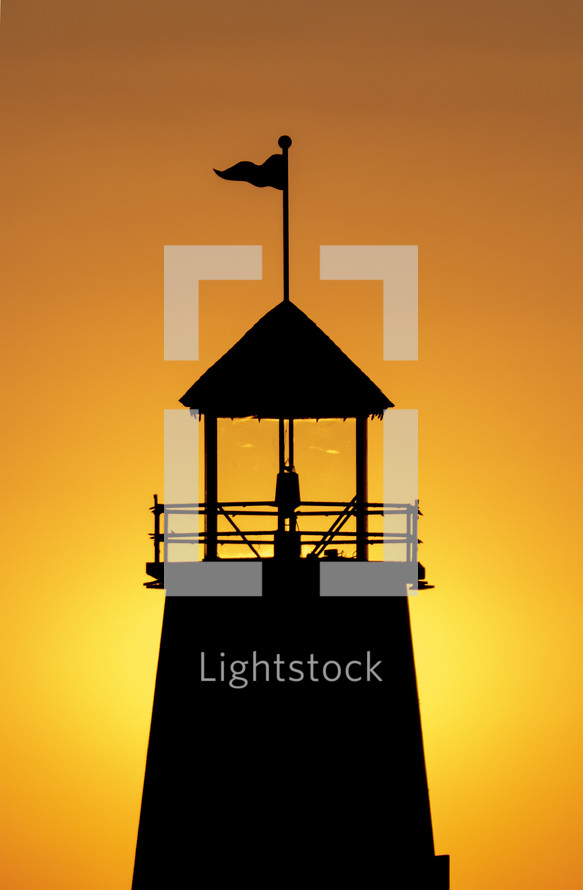 zoomed in view of top of lighthouse with yellow orange sky background at sunset