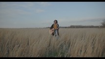a woman standing in a field holding a guitar and singing 