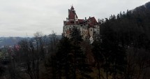 Aerial, rising, drone shot, tilting towards the Bran castle, home of the Dracula legend, on a foggy, overcast, fall day, in Transylvania, Romania
