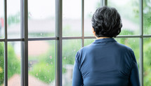 woman with back to the camera looking out a window on a rainy day