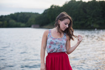 a brunette touching her hair standing in front of a lake 