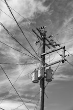 Telephone pole, transformers and electrical wires against a cloudy sky.