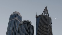 Moon behind skyscrapers, buildings in downtown city of Dubai.