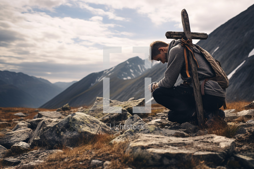 Man kneels with cross on back to pray in mountains