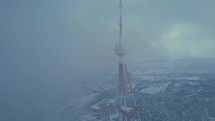 Communication mast in the clouds above the snowy city