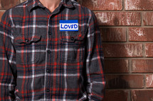 a torso of a man in a plaid shirt with a name tag that reads love 