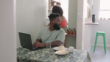 black male freelancer  working online at laptop. Wife support and serve juice to his husband. Online education, work concept.