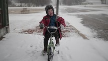 Cut, happy little boy on bike playing outside in snow on cold winter day.