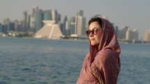 Muslim girl in traditional Abaya dress with Doha skyline behind
