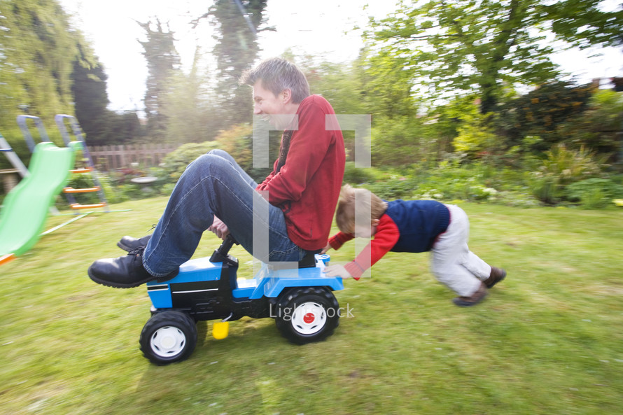 Son pushing his father on a toy tractor in their back garden themes of exhilaration family bonding