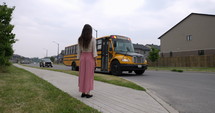 Mother waits as he children arrive on school bus in suburban neighbourhood