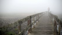 a man walking down a boardwalk on a foggy morning 