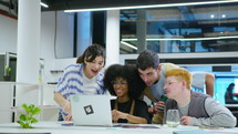 Young multi-ethnic coworkers using laptop, having talk and smiling, working in team on startup business project in modern office
