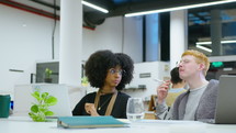 Gen Z multi-ethnic male and female coworkers sitting at workplace in open space office, using laptop, having discussion about business
