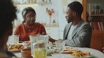 Young joyous African American man and woman having conversation and laughing during family dinner at home
