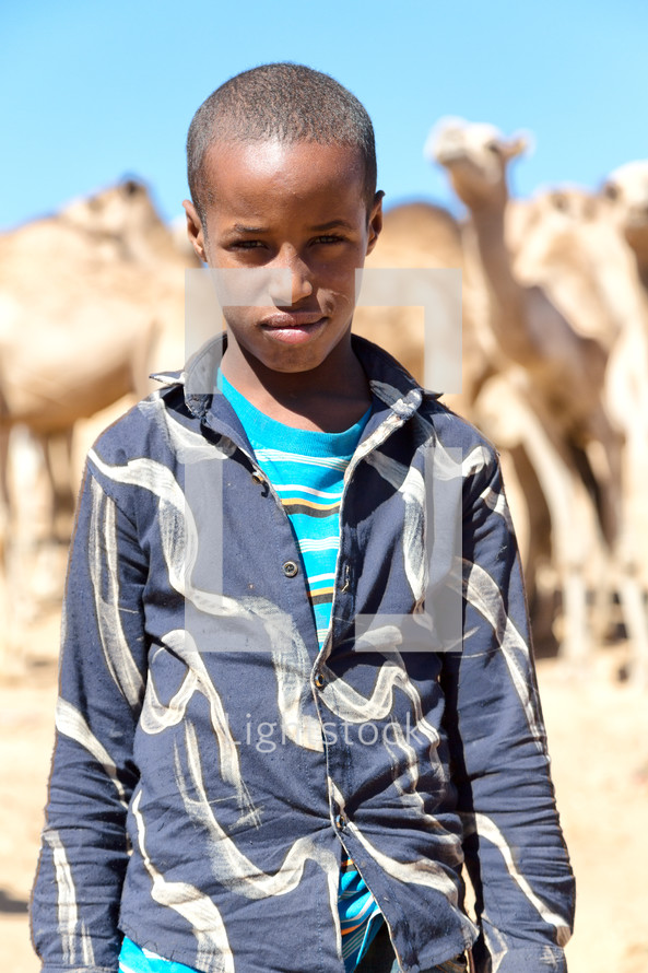 boy in Africa standing with camels 