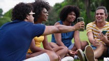 A Group of Multiethnic Young friends sitted in the Park, Talking and Laughing. Diverse Friends watching funny videos on mobile smartphone