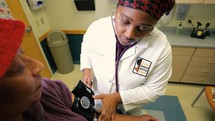 African American woman doctor checking patient blood pressure 