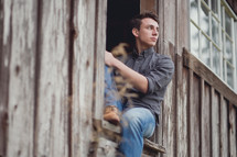 young man sitting in a barn window 