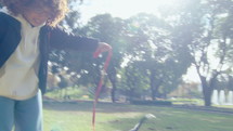 Young woman with curly-hair playing tug-of-war with excited mixed-breed dog, having fun outdoors in the park on a sunny day. Handheld camera shot
