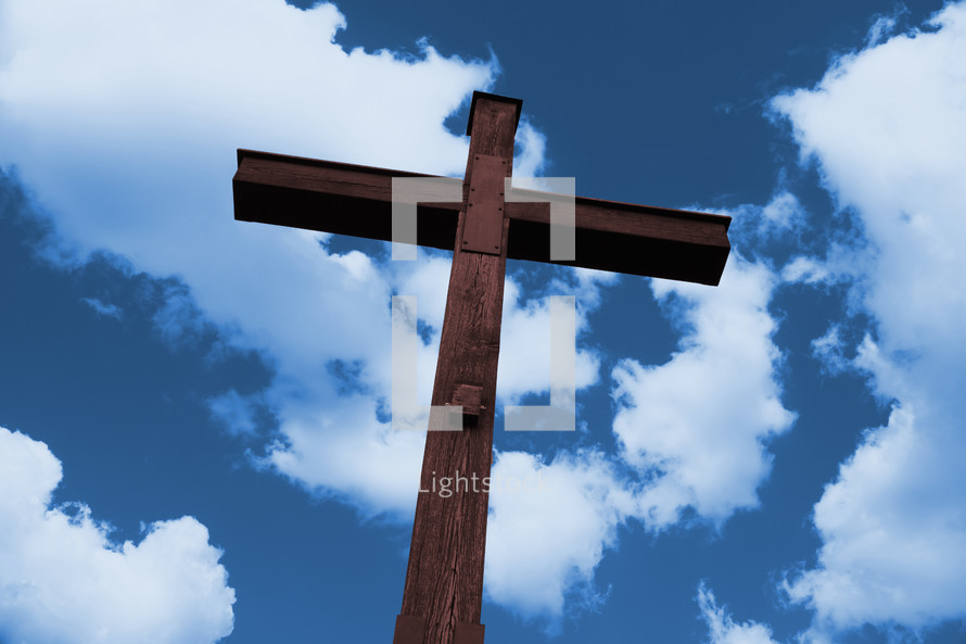 cross of brown wood against white clouds in blue sky