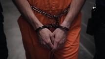 Prisoner shackled in handcuffs and wearing orange prison uniform is led in cinematic slow motion to his prison cell by prison guards.