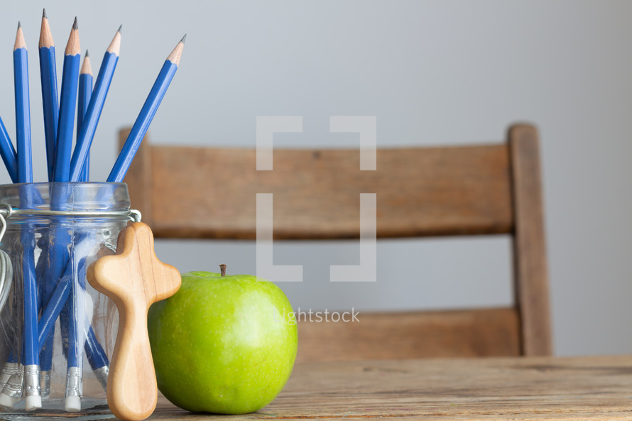 cross, pencils in a jar and apple on a desk 