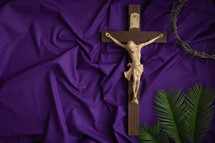 Crucifix, crown of thorns  and palm leaves on a purple cloth 