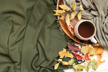 mug on a tray, fall leaves on a green scarf  