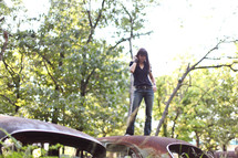 woman standing on old rusted cars in a junk yard