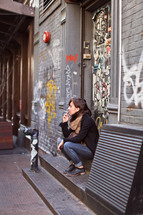 woman siting in front of a graffiti covered wall smoking a cigarette 