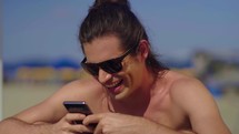 relaxed caucasian man hold use smart phone watching social media sitted at the beach 