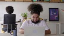 Black African American Man Having an Online Conversation on a Laptop Computer in Creative Office Environment. Happy Male is Browsing Social Media and Replying to Friends in Messenger.
