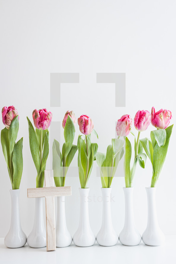 Row of single pink tulips in white vases and cross on a white background with copy space