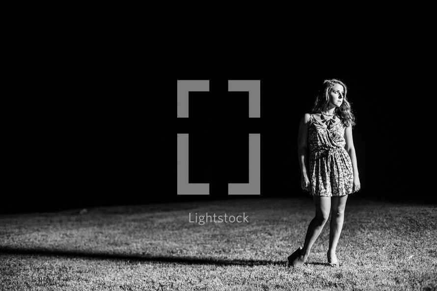 Teen girl standing in a field of grass at night.