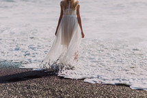 a woman in a flowing sheer dress standing in the tide of the ocean 