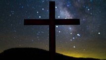 Timelapse of cloud and star movement  over a silhouette of a cross on a hill.